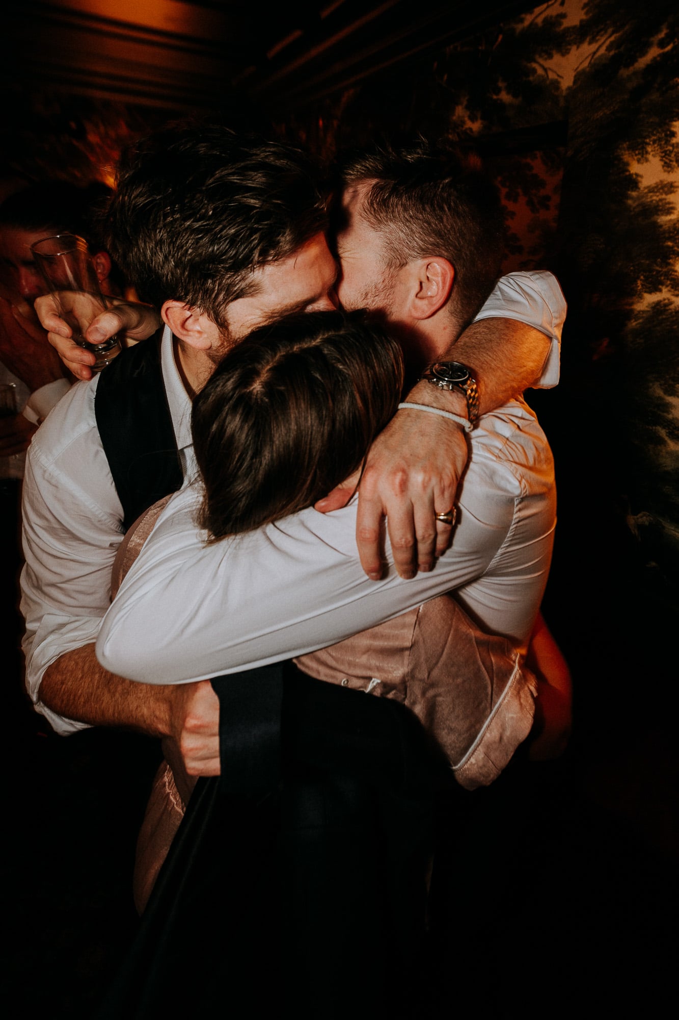 The groom, a glass in his hand, and his friends hug at the party