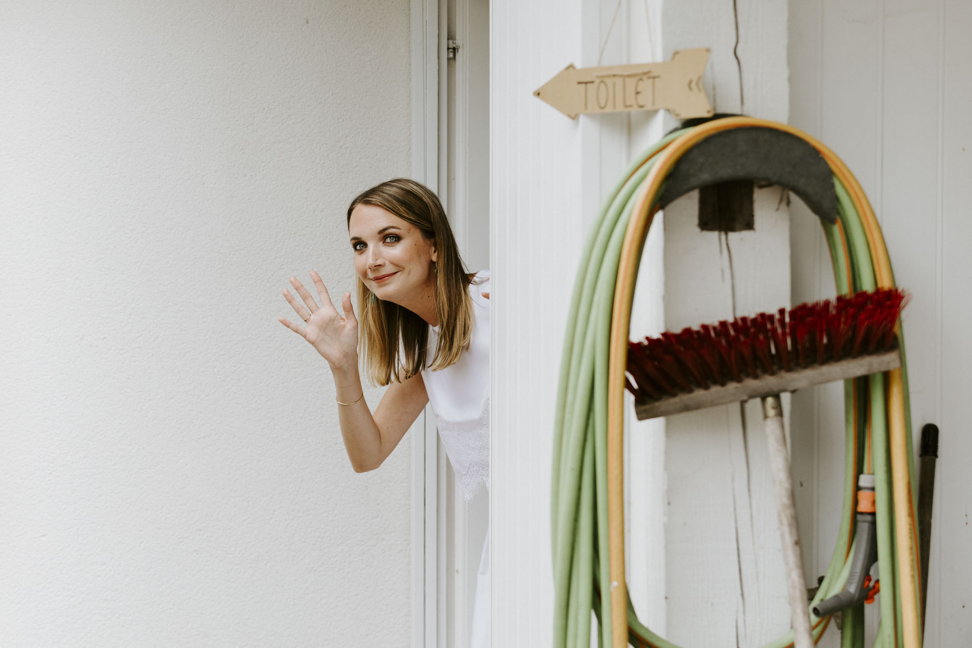 Wedding in Arcachon, France: the bride appears behind a sign that points to the toilets