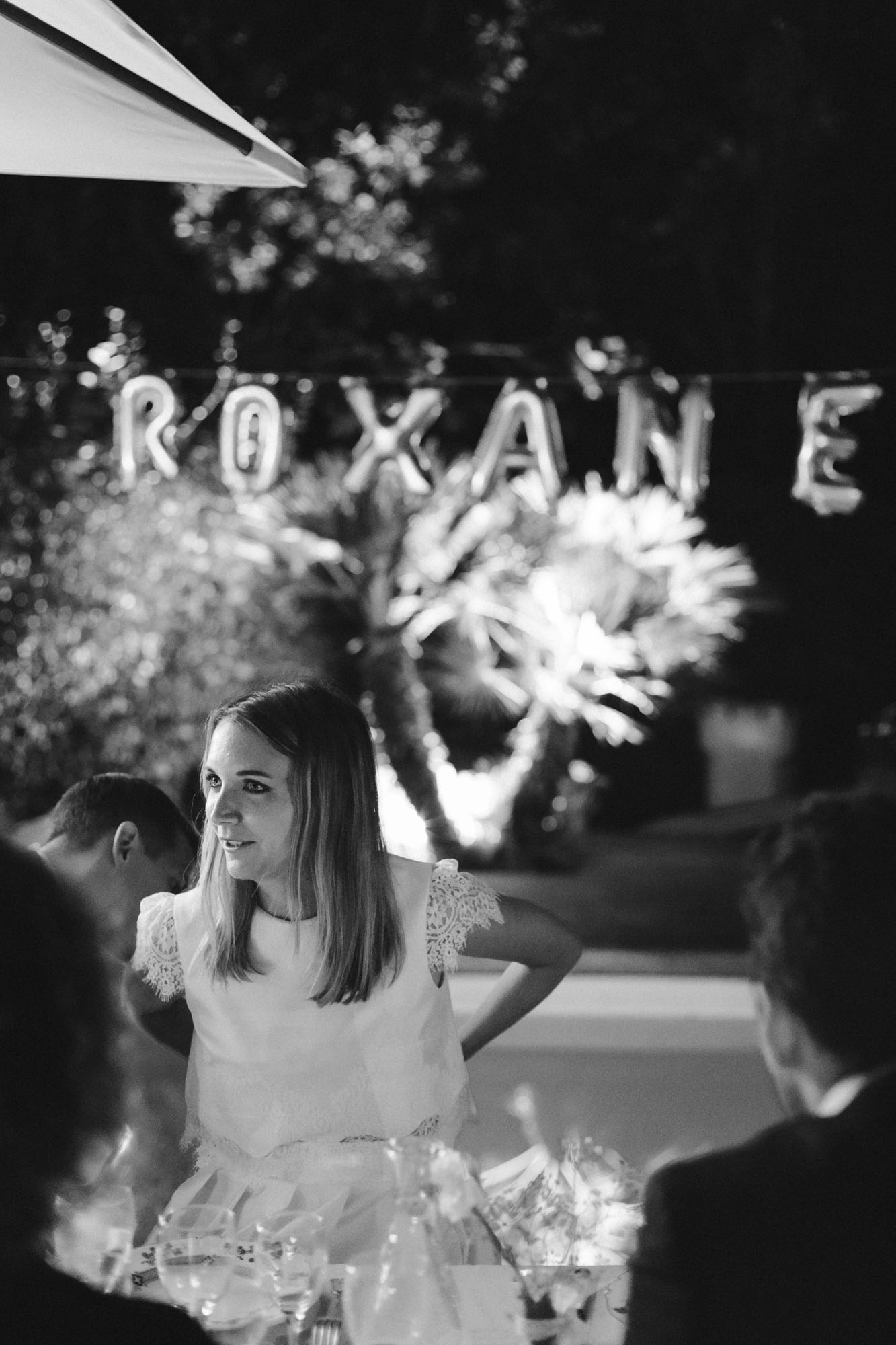 Bordeaux wedding photographer: the bride sits at the dinner table, in the background her name is written in golden letter balloons over the swimming pool of this Arcachon home