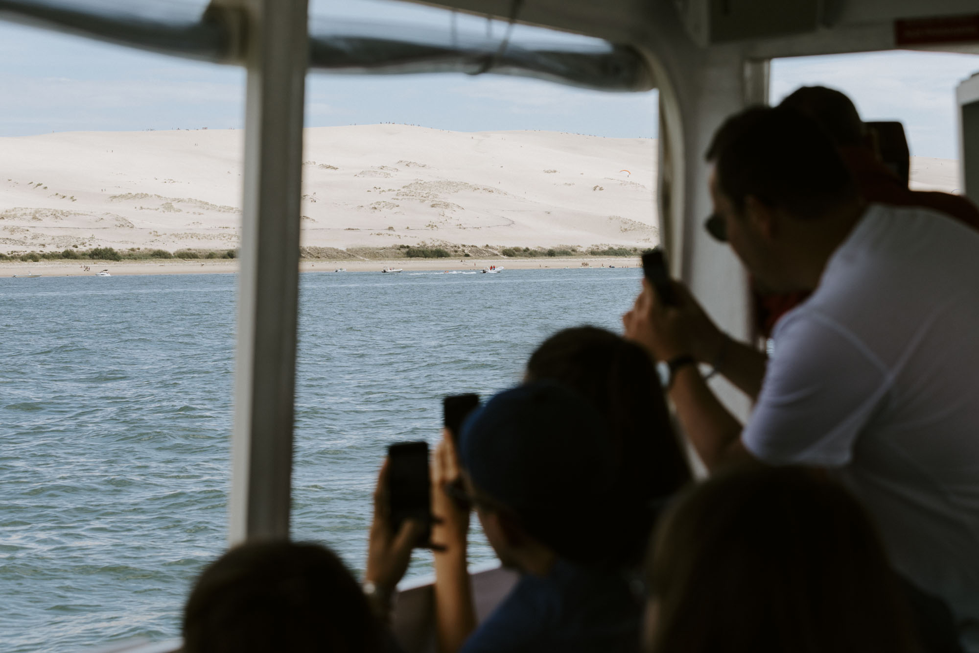 Arcachon wedding photographer: the bay boat is sailing at the botton of Dune du Pyla and all the wedding guests take this opportunity to take pictures of the famous landmark