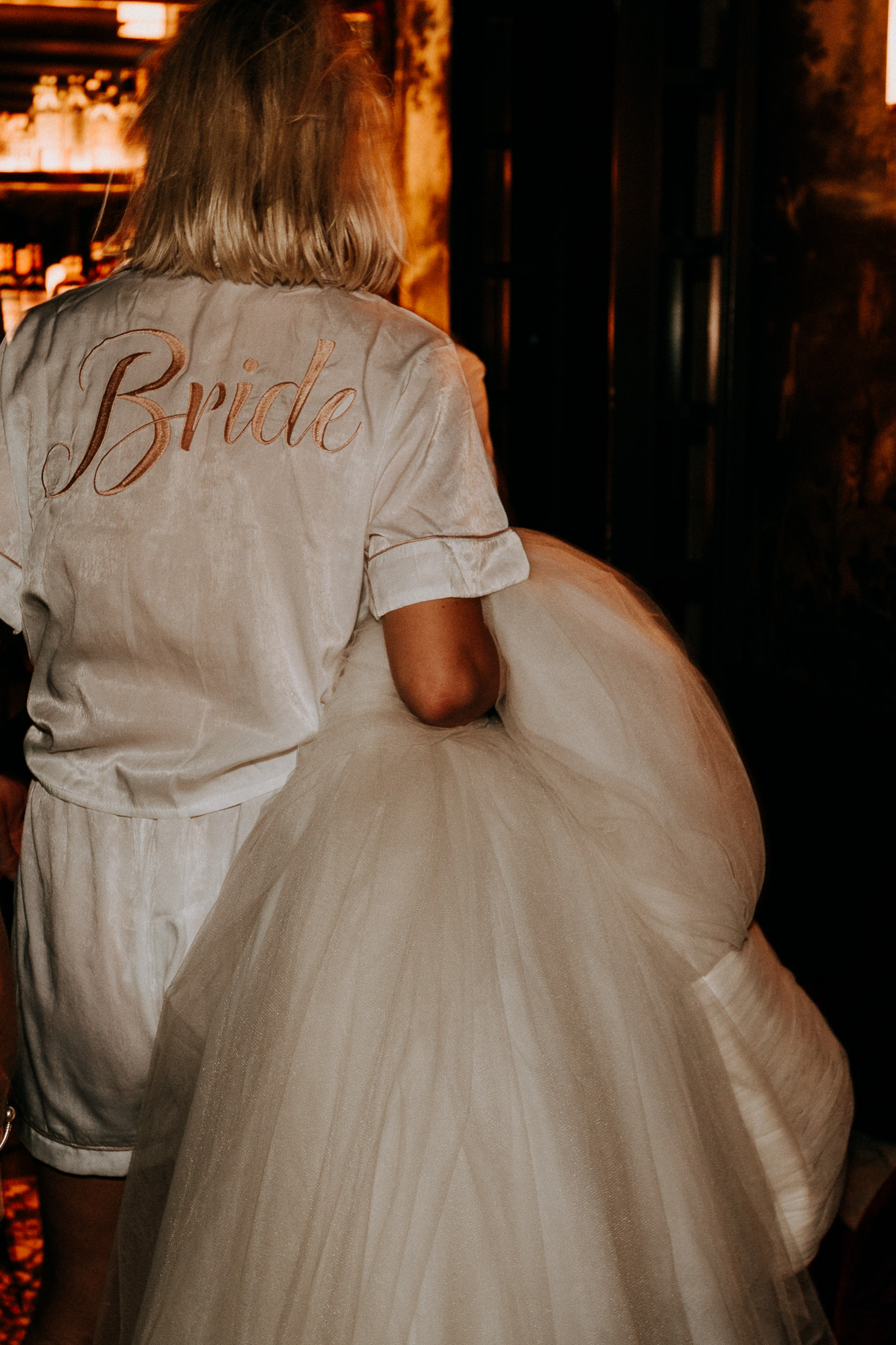 la mariée porte sa robe qu'elle a échangée contre son pyjama en satin avec l'inscription "bride" inscrite sur le dos