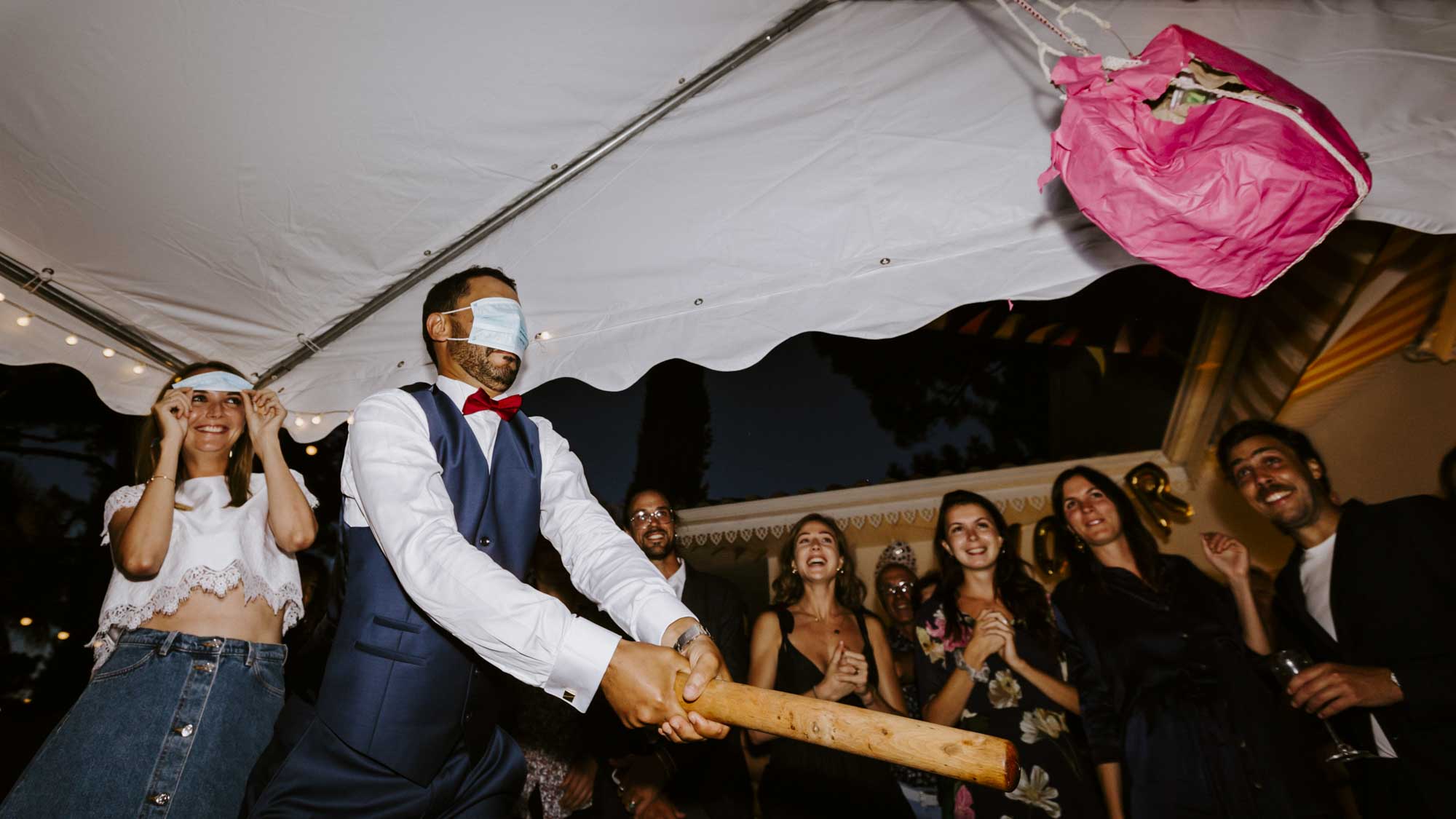 Mariage à Arcachon: le marié, les yeux bandés par un masque chirurgical, tape aveuglement sur une piñata préparé par les invités